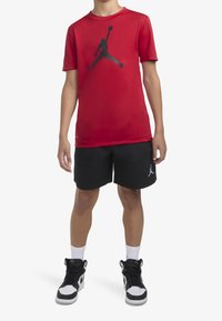 Camiseta atlética roja de manga corta con un logo gráfico negro, combinada con pantalones cortos negros que presentan un logo, y zapatillas altas en blanco y negro.