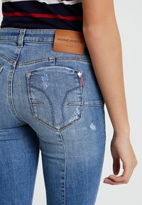 Modré džínové kalhoty s klasickým pětipocket designem, mírným opráním a hnědou koženou zadní nášivkou s vyraženým logem.