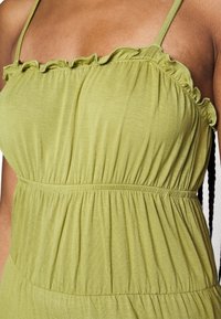 Robe d'été vert olive avec un col froncé, taille élastique et tissu fluide, dotée d'une texture douce et de plis délicats.