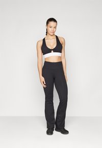 Black sports bra with a white band and keyhole detail, paired with black fitted pants. Smooth texture and streamlined design.