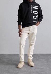 Sudadera con capucha negra con estampado blanco "ICON"; combinada con pantalones de algodón beige y zapatillas de color beige claro. Diseño simple, ajuste informal.