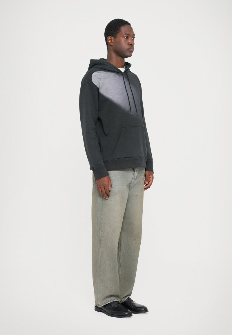 Schwarzer Hoodie mit einem grauen Farbverlauf auf der Vorderseite, Kängurutasche, kombiniert mit hellgrauen weit geschnittenen Jeans und schwarzen Schuhen.