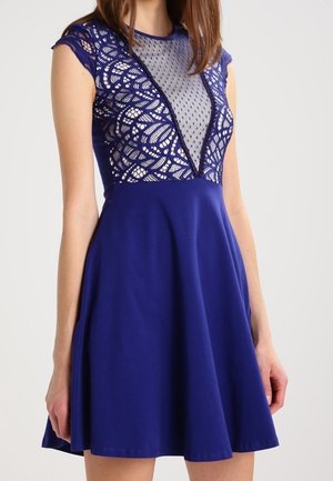 Das blaue Kleid verfügt über ein tailliertes Spitzenoberteil mit V-Ausschnitt und kurzen Ärmeln, ergänzt durch einen ausgestellten Rock. Durchgehend glatte Textur.