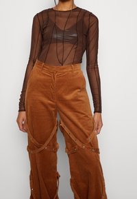 Bruine corduroy wijde broek met een textuurpatroon, voorzien van zilverkleurige metallic details en uitsparingen, gecombineerd met een doorschijnende zwarte lange mouw top.