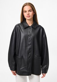 Schwarze Kunstleder-Übergangsjacke im Oversized-Stil mit umschlagbarem Kragen, Knopfverschluss vorne und zwei Klappentaschen. Glatte Textur mit einer lockeren Passform.