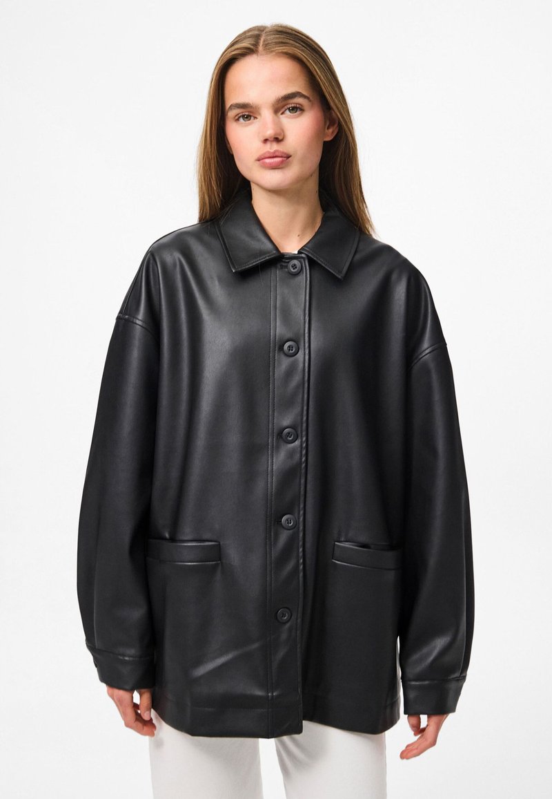 Schwarze Kunstleder-Übergangsjacke im Oversized-Stil mit umschlagbarem Kragen, Knopfverschluss vorne und zwei Klappentaschen. Glatte Textur mit einer lockeren Passform.