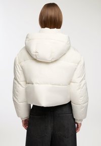 Biała, krótka kurtka puchowa z kapturem, z pikowanymi sekcjami i elastycznymi mankietami. W połączeniu z czarnymi spodniami w wysokim stanie.