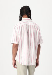 Short-sleeve shirt in white fabric with red and blue vertical stripes, featuring a button-down collar and a relaxed fit with side slits.