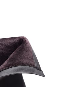 Czarny skórzany produkt z miękkim, puszystym fioletowym wnętrzem. Posiada złożony design i gładką, zaokrągloną krawędź. Widoczny jest teksturowany detal materiału.