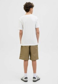 Valkoinen lyhythihainen t-paita yhdistettynä oliivinvihreisiin shortseihin. Shortseissa on kevyt kangas ja rento malli. Mustat ja valkoiset lenkkarit.