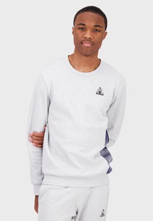 Sudadera gris de cuello redondo con un pequeño logo negro en el pecho y acentos de rayas azules a lo largo de las mangas, hecha de un suave material de algodón.