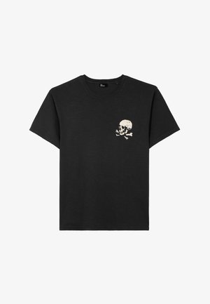 T-shirt en coton noir à manches courtes et col rond. Présente un motif blanc de tête de mort avec des os croisés sur le côté gauche de la poitrine.