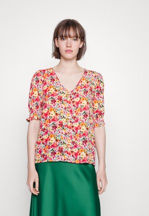 Blusa floral com decote em V, mangas curtas bufantes e um padrão colorido de flores rosas, amarelas e verdes sobre um fundo claro.