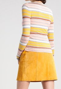 Geripptes Sweatshirt mit vertikalen Streifen in Rosa, Gelb, Grau und Orange, kombiniert mit einem gelben Wildleder-Minikleid mit glatter Textur.