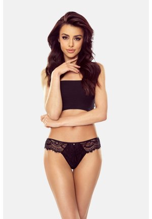 Schwarzer Spitzen-Thong mit floralen Mustern, ausgestattet mit einem glatten Bund und dekorativen Akzenten. Das Model posiert mit verschränkten Armen und trägt ein passendes Crop-Top.