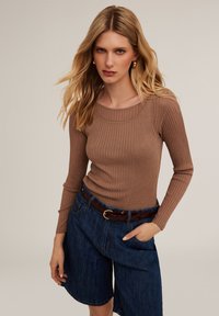 Bruine geribbelde lange mouw top gecombineerd met high-waisted denim shorts en een bruine riem. Zachte textuur, ronde halslijn, losse pasvorm.