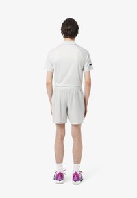 Conjunto deportivo de color gris claro que incluye una camiseta de cuello y mangas cortas, y pantalones cortos con cintura elástica, combinados con zapatillas con acentos morados.