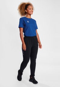 Blå t-shirt med rund hals og logo, parret med sorte joggingbukser med et sideskiltmønster og elastisk talje. Svarte sneakers fuldender looket.