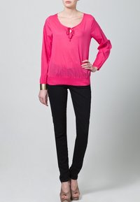 Ljusrosa långärmad blus med rundad hals och knytdekor, ihop med figursydda svarta byxor och beige högklackade skor.