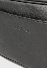 Crna kožna torba s teksturiranim površinom, prošivenim detaljima i urezanim brendom "LES DEUX" sa strane. Minimalistički dizajn.