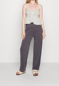 Ljusgrå croppad topp med justerbara axelremmar och rynkad framtill, i kombination med lösa, mörkgrå byxor och avslappnade beige sandaler.