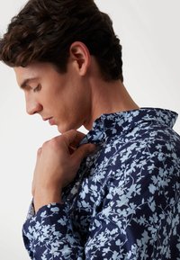 Camicia blu navy con un motivo floreale in azzurro chiaro. Presenta un colletto classico e maniche lunghe. Tessuto morbido e confortevole.