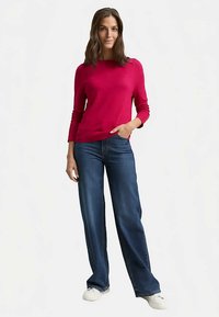 Maglione fucsia a maniche lunghe abbinato a jeans a gamba larga di colore blu scuro. Il maglione presenta una scollatura arrotondata e maniche aderenti; i jeans hanno una vestibilità comoda.