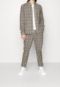 Brun och krämfärgad rutiga skjorta med matchande byxor, i avslappnad passform och vita sneakers. Tyget har en slät yta.