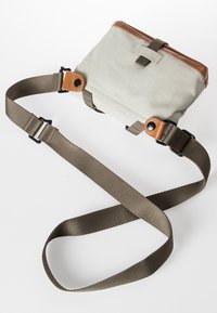 Borsa di colore crema con un accento in pelle marrone, tracolla regolabile e chiusura a patta. Texture liscia, forma rettangolare.