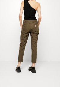 Olijfgroene, taps toelopende broeken met elastische tailleband, achterzakken en geborduurd logo. Gemaakt met een gestructureerd zwart, één-schoudertop.