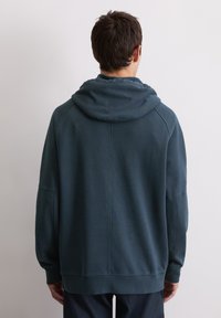 Sweatshirt bleu foncé à coupe décontractée, doté d'une grande capuche douce et de manches côtelées. L'arrière présente un design avec des coutures décoratives.