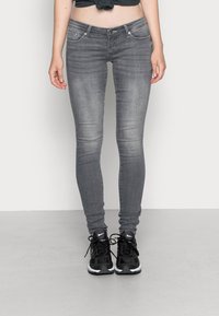 Jeans gris ajustados con una textura suave, diseño de cinco bolsillos y un ligero desgaste. Llevados con zapatillas deportivas negras.
