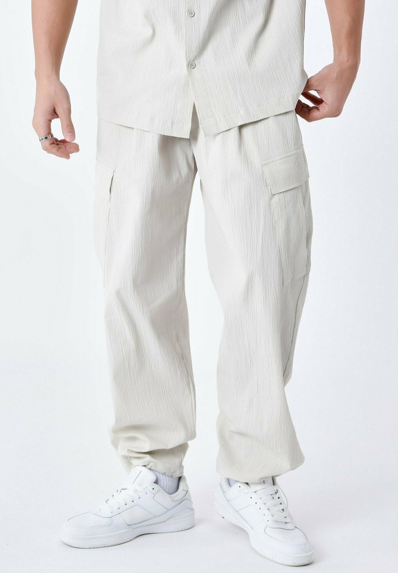 Beige cargo bukser med en tekstureret finish, der har sidelommer og en afslappet pasform. Kombineret med hvide sneakers.