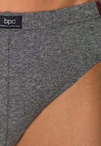 Pantaloni grigi realizzati in un morbido tessuto con finitura testurizzata, dotati di un'etichetta con logo e una sottile cucitura rossa sulla vita.