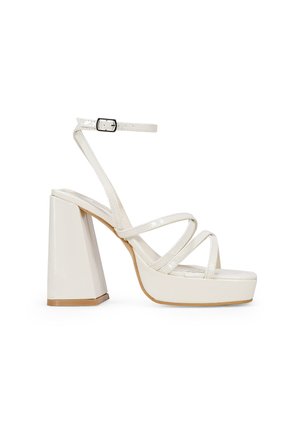 Sandal de tacón alto de charol blanco con un chunky block heel, tiras delgadas entrelazadas y correa de tobillo ajustable. Acabado suave y diseño de plataforma.