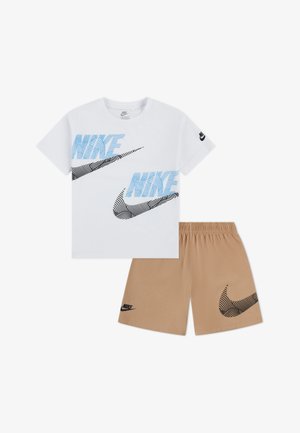 Hvit T-skjorte med blå og svart grafisk tekst og Nike-logo; kombinert med beige shorts med svart Nike-logo og mønster.