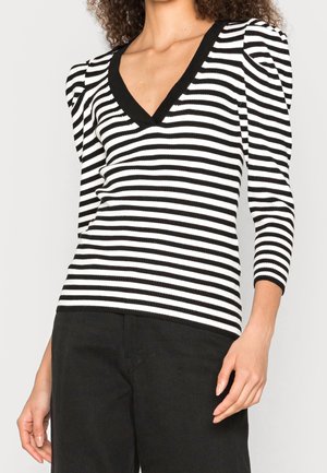 Haut en tricot rayé noir et blanc avec un décolleté en V profond, des manches bouffantes et une texture côtelée. Associé à un pantalon noir.