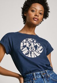 Camiseta de algodón azul marino con mangas enrolladas y un diseño gráfico circular blanco con texto estilizado en el centro.