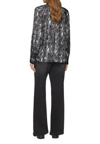 Chemise à boutons en imprimé serpent noir et blanc, avec des manches longues, associée à un pantalon large foncé. Tissu lisse, coupe décontractée et détails minimalistes.