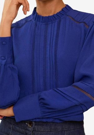 Blå bluse med et tekstureret design med lodrette plisséer, rynket halsudskæring og puffede ærmer med detaljerede accenter og gennemskinnelige paneler.