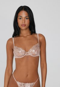 Koronkowy stanik w delikatnym beżu z kwiatowym haftem, z fiszbinami i regulowanymi ramiączkami. W komplecie przejrzysty thong.