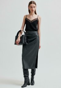 Kivimust tank top, millel on läbipaistev V-kujuline kaelus, koos kõrge vöökohtadega musta nahkse seeliku ja külje lõhiku ning rihmadega mustade kontsakingadega.