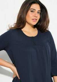 Tunic blu navy con scollatura arrotondata, patta con tre bottoni e pieghe nella parte inferiore. Tessuto morbido e maniche a tre quarti.