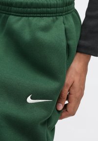 Πράσινο παντελόνι φόρμας Nike με ελαστική μέση και πλαϊνές τσέπες. Διαθέτει μικρό λευκό κεντητό λογότυπο Nike στο μηρό. Μαλακή υφή.