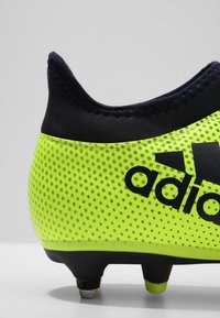Kopačky Adidas na fotbal s jasně žlutým síťovaným svrškem, námořnickým límcem a výrazným černým logem. Obsahují tvarované kolíky pro trakci.