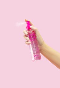 Spruzzatura a mano di una bottiglia trasparente rosa di mist per il viso e abbronzante alla rosa su uno sfondo rosa chiaro.