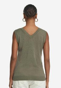 Lätt, ärmlös v-ringad tröja i olivgrön. Har en ribbad nederkant och en avslappnad passform med en slät textur.