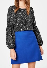 Blusa nera con motivo floreale bianco, dotata di maniche a palloncino. Abbinata a una mini gonna A-line blu brillante, entrambe in tessuto morbido.