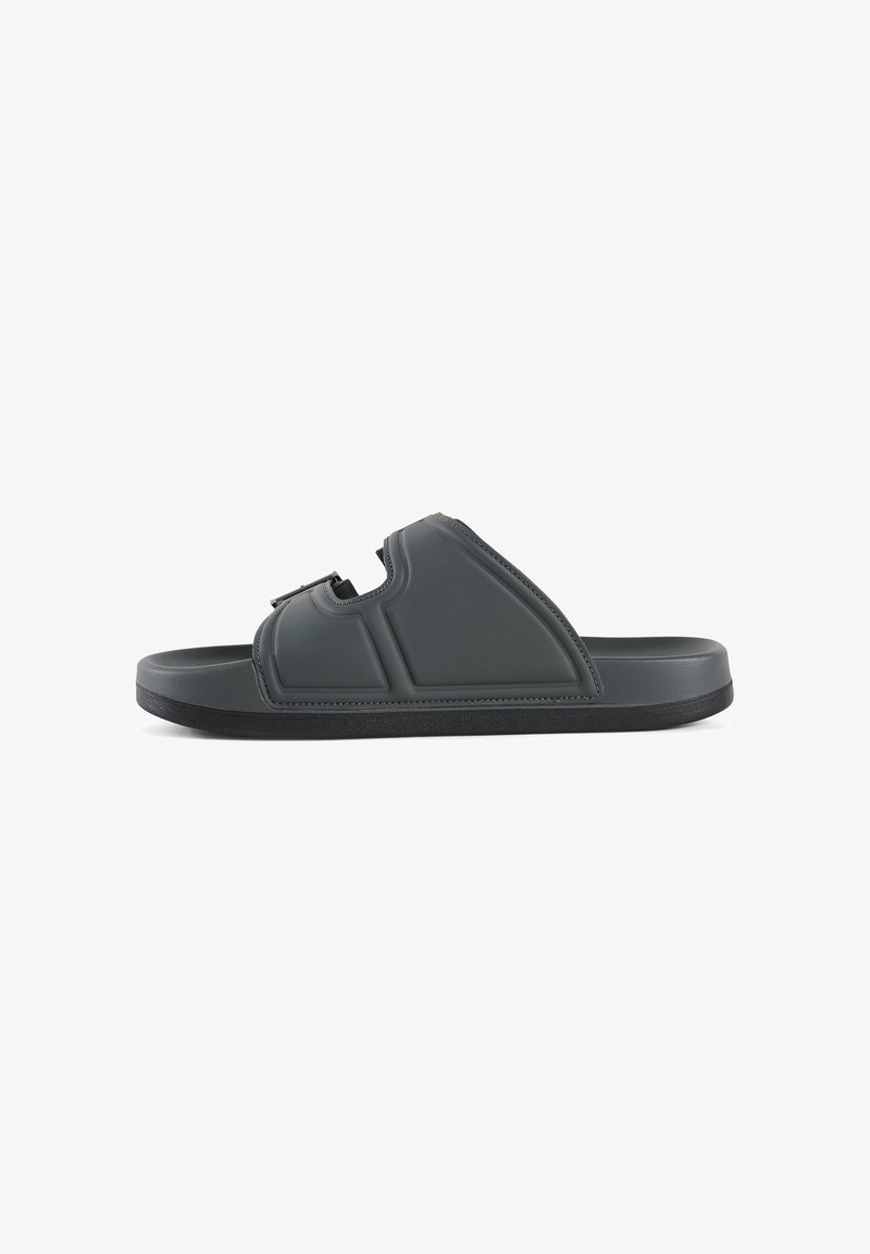 Sandalia de slip-on de color gris oscuro hecha de plástico suave. Cuenta con una sola correa ajustable y una suela texturizada para mayor agarre. Forma contorneada con acolchado.