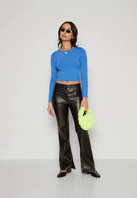 Plavi dugi rukav krojeni crop top, crne hlače od faux kože s trumpom, zelena torba od faux krzna i crne balerinke. Minimalni dodaci i sunčane naočale.